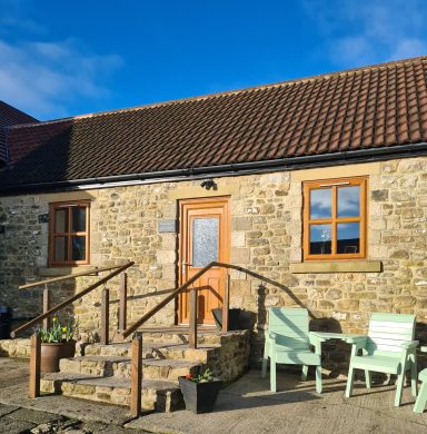 Stone cottage with a wooden door, steps, and two mint green chairs outside.