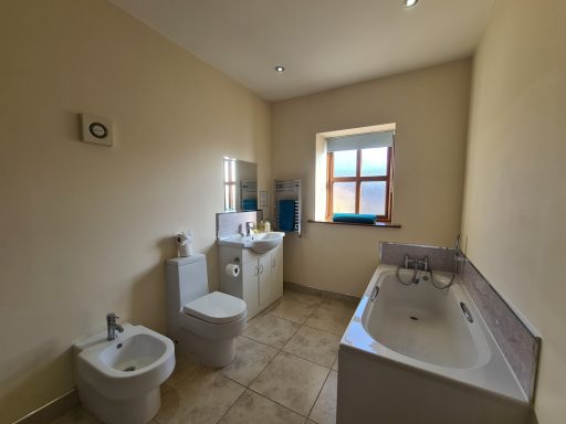 Bright bathroom with a bathtub, bidet, toilet, and a window.