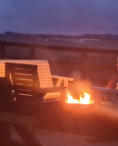 A firepit burns warmly beside a chair on a dimly lit outdoor patio.