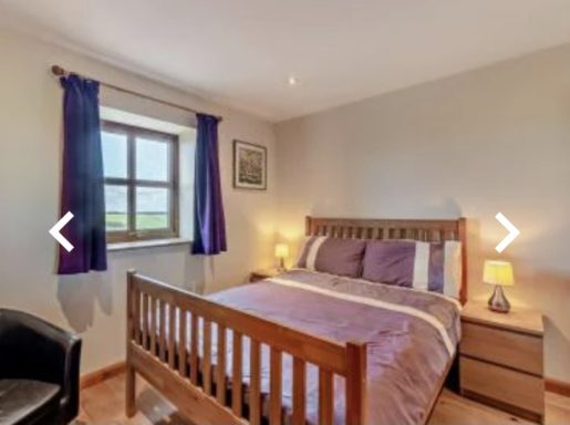 A cosy bedroom with a double bed, chair, and a window letting in natural light.