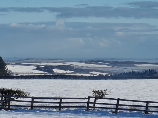 Snow-covered landscape with rolling hills and a wooden fence in the foreground.