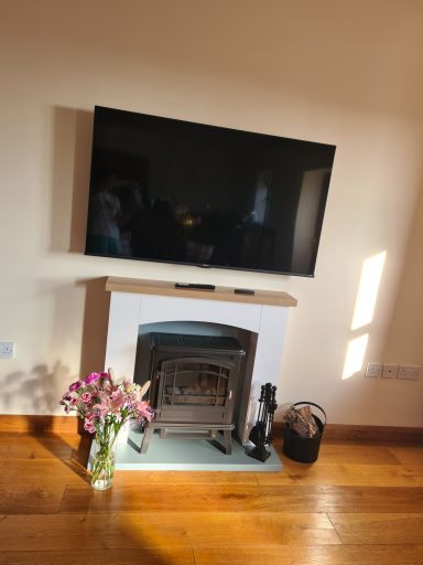 Modern living room with a TV above a stylish fireplace and a vase of flowers on the side.