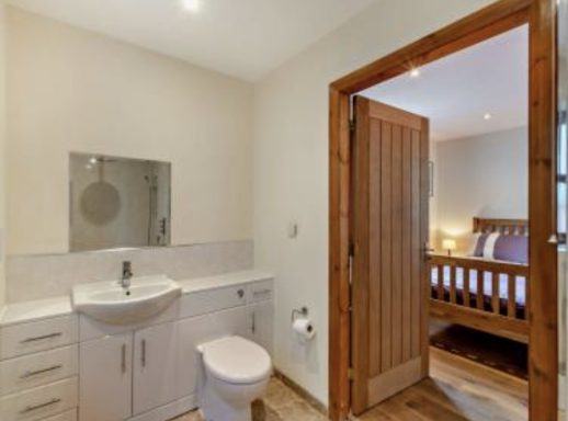 Modern bathroom with sink and toilet, adjoining a softly lit bedroom.