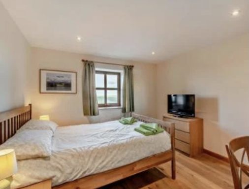 Cozy bedroom with a double bed, green curtains, a TV, and wooden furniture.