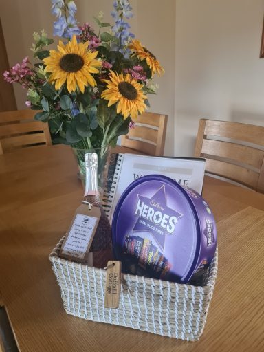 A gift basket with chocolates, a notebook, and a vase of sunflowers.