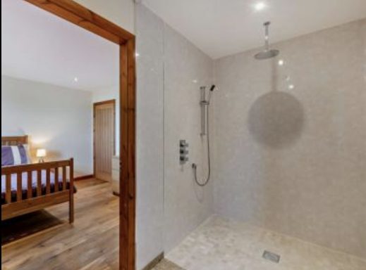 Corner shower area with modern fixtures, adjacent to a wooden bed and bedroom entrance.