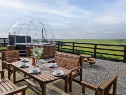 Outdoor dining area with a wooden table, chairs, and a clear dome overlooking a scenic landscape.