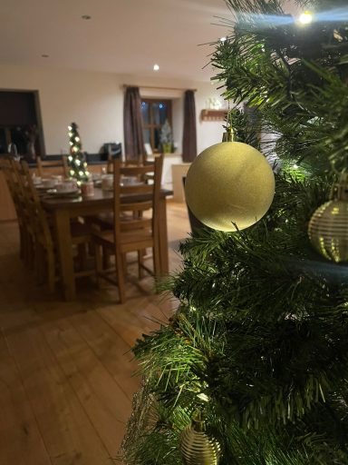 Decorated Christmas tree with gold ornaments in a warmly lit dining area.