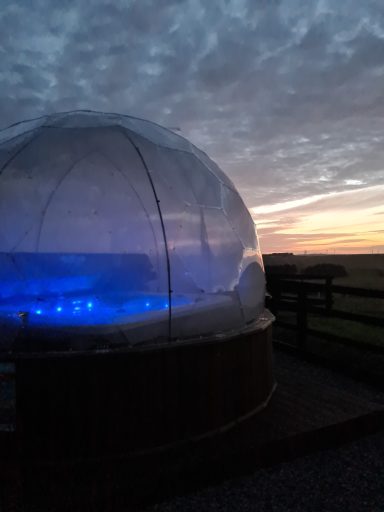 A clear dome structure with blue lighting against a sunset sky.