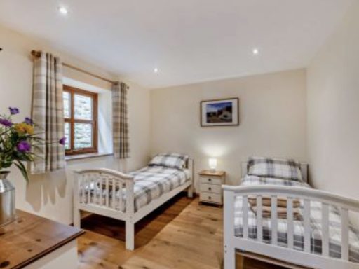 Bright bedroom with two single beds, wooden flooring, window, and decorative flowers.